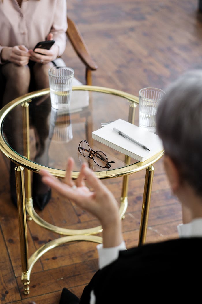 our-services-2 Two adults engaged in a therapy session, seated at a glass table with notebooks and water glasses.