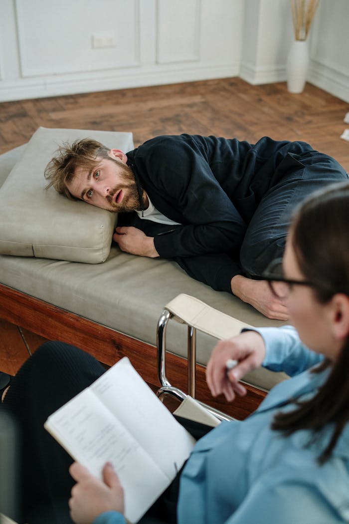why-choose-us A bearded man in therapy session lying on a couch indoors with a therapist writing notes.