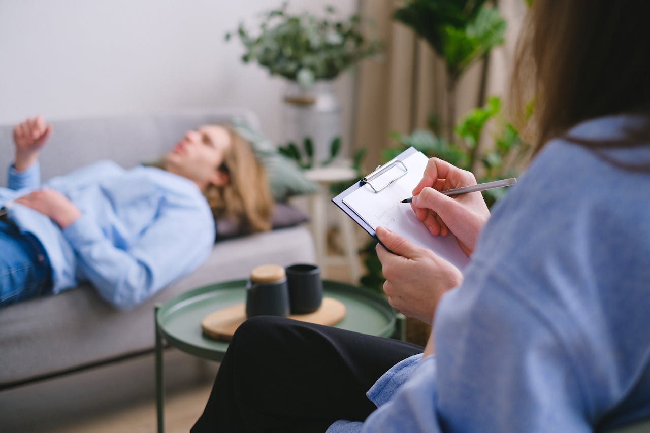 our-services-3 A therapy session in progress with a therapist taking notes as a patient reclines on a sofa.